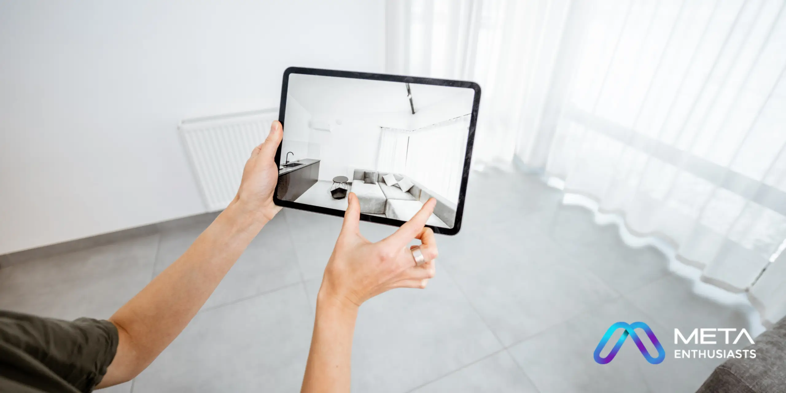 Person holding a tablet displaying an augmented reality view of a furnished room in a bright, empty space. "Meta Enthusiasts" logo is visible in the lower right corner, showcasing their innovative use of augmented reality technology.